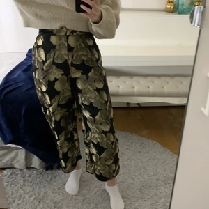 Blommiga byxor i guld och svart - Ett par coola blommiga byxor i svart och guld från Lindex 🌼🖤 Storlek 36 som motsvarar ungefär en S. Säljer pga att de är för korta för mig som är 169 cm lång. Köparen står för frakten, 62 kr, eller så kan jag mötas upp i Gävle📬🤗 Pris 100 kr exklusive frakt