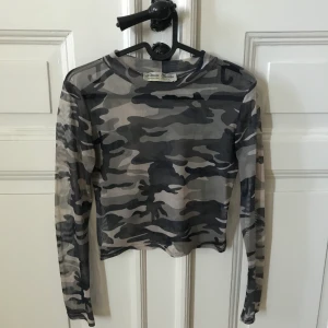 Militärmönstrad Mesh Tröja - Militärmönstrad mesh tröja från Whoops! Köpt för rätt många år sedan så finns nog ej kvar. Långärmad och croppad till strax under naveln. Står ej strl men gissar på S/M! Använd fåtal ggr men i jättebra skick. Som ni ser på bild 2 är den rätt see-through pga tyget men skitsnygg med ett linne under om man inte vill visa för mycket!🥰