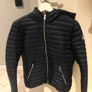Colmar tunn dunjacka - Säljer min marinblåa colmarjacka (beige insida och mörk logga) Väldigt fint skick!! Köpt på rea för 2449kr men annars är nypris 3599kr💖 Säljer den för 750kr och köparen står för frakten✨✨ Storlek 44 (italiensk storlek om jag minns rätt, motsvarar Small/Medium)