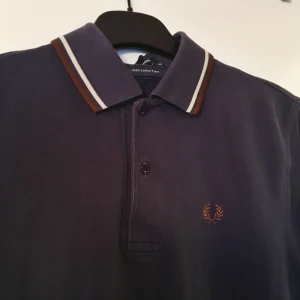  - Fred Perry-pike! Mörkblå med vita och bruna streck.  Storlek XS (man) Frakt inkluderat i pris :)