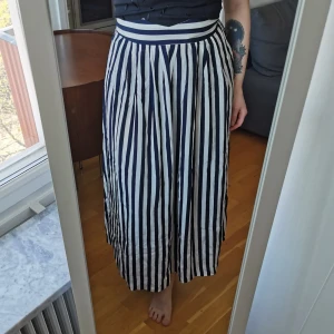 Randig kjol - Blå/vitrandig långkjol med schysst vidd. Supersnygg med bara en enkel body till! Uppskattningsvis strl XS/S. Mått: midja 36 cm, längd 91 cm. Dragkedja och knapp baktill. Köparen står för porto 63 kr (spårbart) 