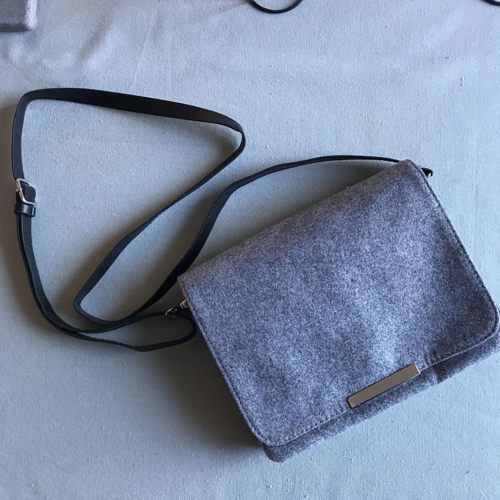 Helt oanvänd handväska i mjukt grått tyg, flera fack och justerbar rem. Väskor.