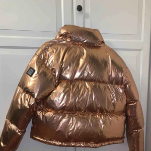  - Varm och skön vinterjacka från Tommy Hilfiger (denim). Färgen är en glansig koppar/guld färg. Nypris : 3000 SEK.  Använd ett fåtal gånger pga den inte är min stil. Hög krage ingen luva. Kan mötas i Stockholm annars står köparen för frakten.