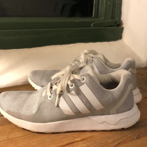 Adidas sneakers  - Gråa sneakers med vit sula från adidas. Mycket fint skick då de knappt är använda. Det enda som syns är att Adidasmärket på framsidan på andra bilden är lite sönder, dock inget man tänker på. 