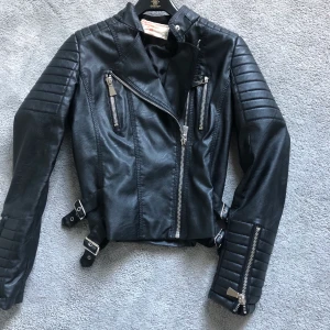 Skinnjacka från chiquelle  - Svart Skinnjacka, i fake skinn, från chiquelle med silvermedaljer. Storlek 38 men liten i storleken. Passar 34-36. Frakt tillkommer på 99kr