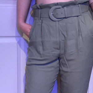 Gröna byxor från &Otherstories - Ljusgröna högmidjade kostymbyxor från &Otherstories med brett bälte i midjan. Köparen står för frakten! 🤩