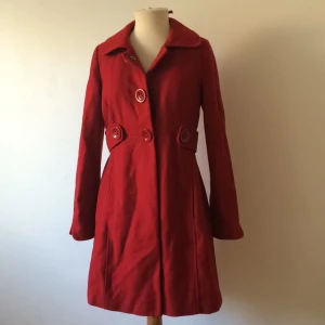  - Romantisk röd kappa perfekt för alla typer av tillfällen. Innerficka samt två fickor i sidorna som fortfarande är igensydda. Hängflärpen är tyvärr av.