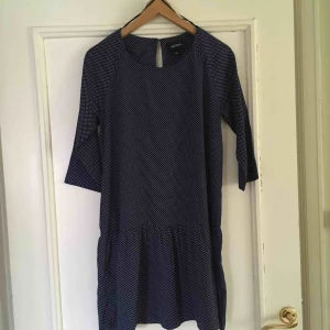  - Tunn klänning från Monki. Mörkblå med vita prickar. Tygstycke längst ned som är lite vidare. Knäpps i ryggen med en knapp. Halvlång ärm. Går ned till ca ovan knäna. 