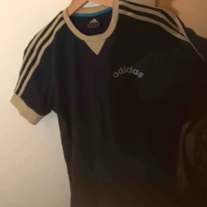  - Snygg adidas tshirt med logga. Köpt secondhand. I bra skick. Beiga detaljer och logga (med ljusare blå kant på bokstäverna), självaste tröjan är mörkblå