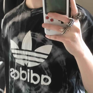  - Ej äkta, men vad gör det? Fett fräsig tie-dyed T-shirt med ADIDAS tryck på :) använde en hel del under två år men är i rätt så bra skick fortfarande. Frakt ingår i priset! 