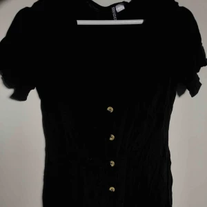  - Söt klänning i svart. Köpt på H&M i prag. Stl 40 men är betydligt mindre. Jag skulle säga 36/38. Bruna knappar, går att knäppa upp hela vägen. Jag är 163, säljer pga för liten.