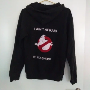  - En svart hoodie/huvtröja/munktröja med fickor fram. Text på framsidan, text och bild på ryggen. Skick: Begagnad. Gratis frakt!