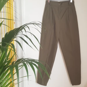 Khakigröna kostymbyxor, stl 36. - Khakigröna kostymbyxor. Hög midja. Pressveck. Mycket bra skick. Ca stl S, benen är långa. Något mer gröna än på bilderna. Frakt tillkommer.