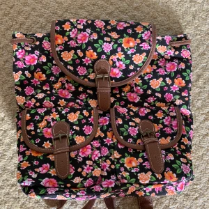 Färgglad ryggsäck - Vacker färgglad ryggsäck, öppnas med knapp 2 fack fram, 1 bak, 1 stort inuti och 1 mindre Köpt i London Aldrig använd, perfekt skick Nypris 599kr