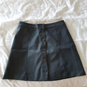 Läder kjol med knappar - En kjol från H&M, jättebekväm med lite olika sätt att använda den (knappar rakt fram, knappar på sidan, några uppknäppta etc), är stl 40 men känns mer som en 38/36 i midjan 