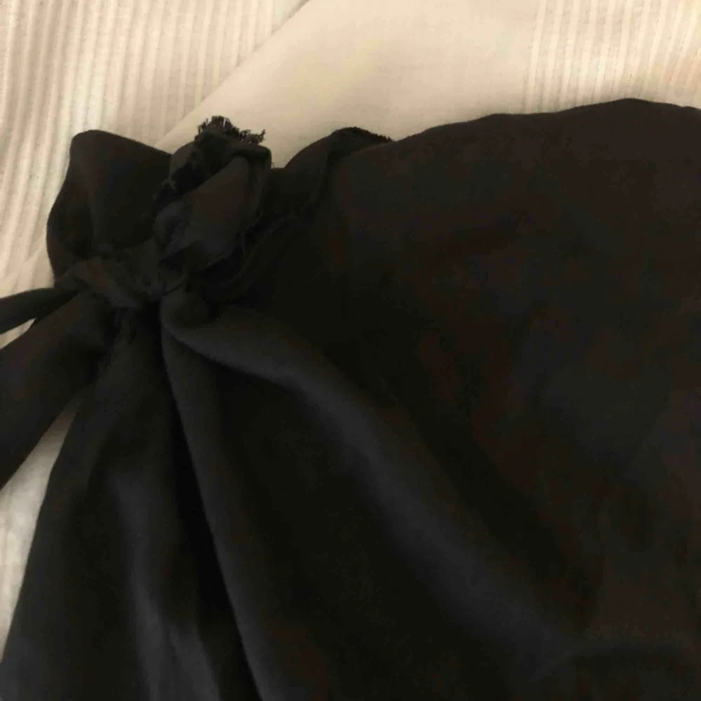 En jättefin svart kjol i tyg som man knyter runt midjan, den har en dragkedja på sidan och är lite halft fransig nere på kanten, använd några gånger men i bra skick, den är i medium men passar även mig som har S. Kjolar.
