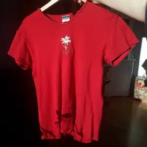 En röd t-shirt med en gullig broderad blomma på. Det står XL men passar mer som en M/L