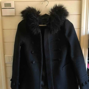  - Svart kappa med luva och svart päls från Zara. Kortare i modellen men väldigt fin på vintern. Försluts med knappar som finns längs med kappan. Köparen står för frakten!