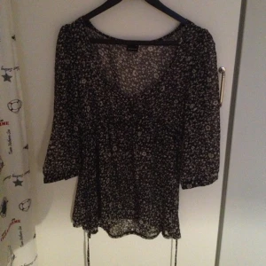 Långärmad sval blus svart/vit-mönstrad med snörning i midjan, svarta knappar. - Långärmad sval blus svart/vit-mönstrad med snörning i midjan, svarta knappar.