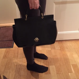  - En väska i äkta skinn från &otherstories i bra skick. Axelrem medföljer. Svart skinn med gulddetaljer