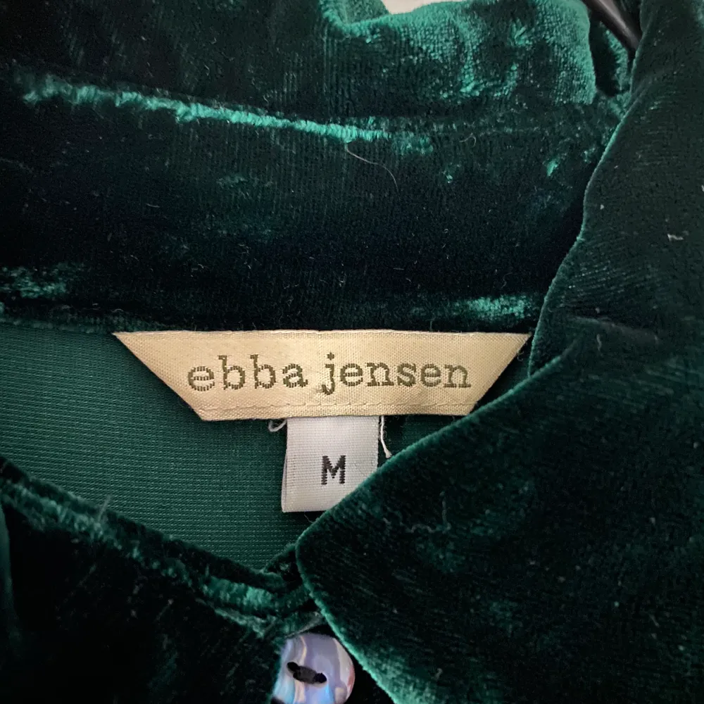 Grön sammetsskjorta från Ebba Jensen i stl M. Av viskos och siden. Bra skick förutom ett litet hål fram på vänster sida (se bild 3). Kan postas mot 55kr porto.. Skjortor.