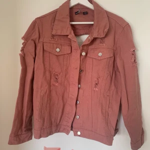 Jeansjacka  - En rosa jeansjacka med slitningar. Stor Slitning i ryggen