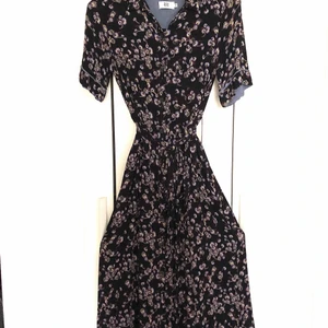 Maxiklänning med vidd och fint fall - Mörkblå botten med blommönster. Fina detaljer, som passpoaler och veck på kragen. Violett foder på insidan av ärmen, även fållen har en violett centimeterbred infodring på insidan. Knäppningen går hela vägen uppifrån och ner. Normal passform, 100 % viskos