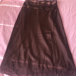 Brun satinkjol med slits  - Brun midikjol i satin med slits och spets nedtill från Vero Moda. Använd någon enstaka gång. Färgen syns bästa på andra/tredje bilden. Frakt tillkommer💗