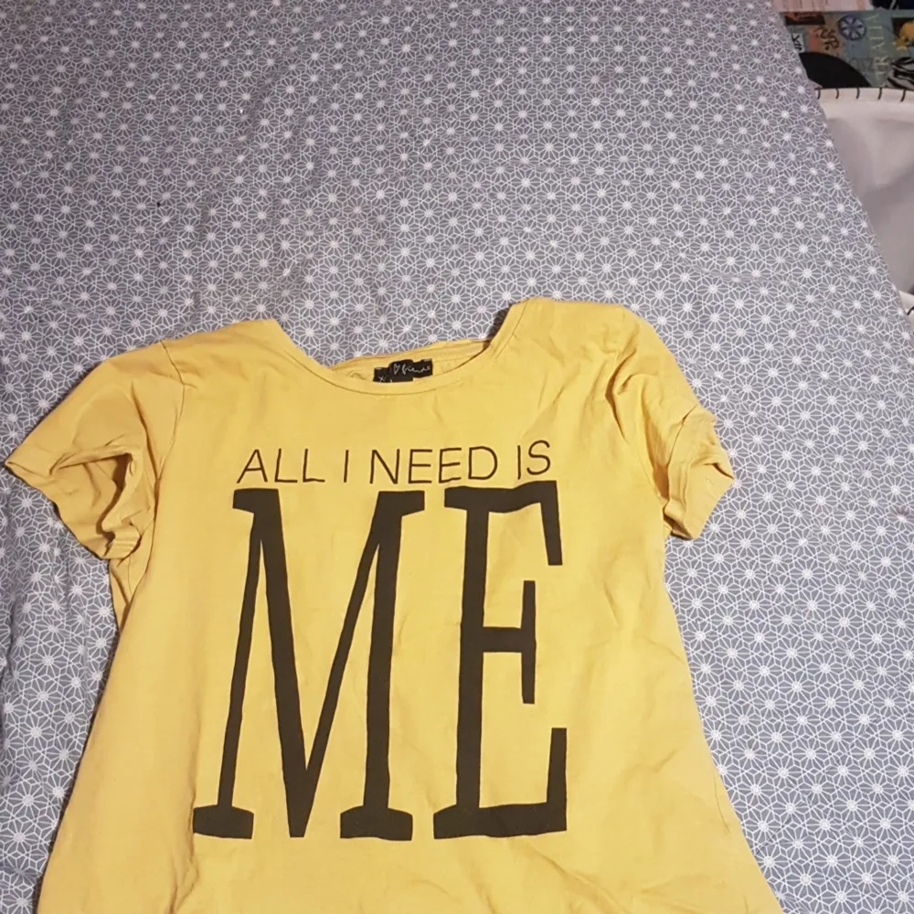 Det är en gul t-shirt med en liten text där det står ALL I NEED I ME. Köparen betalar frakt.. T-shirts.