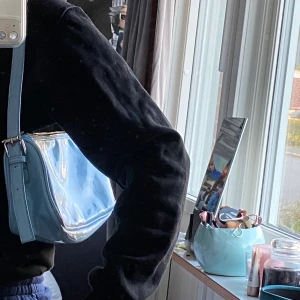 Blå shoulderbag  - En blank shoulderbag i jätte fin ljus blå färg. Den är knappt andvänd, kan mötas upp i Stockholm annars står köparen fär frakten!😁