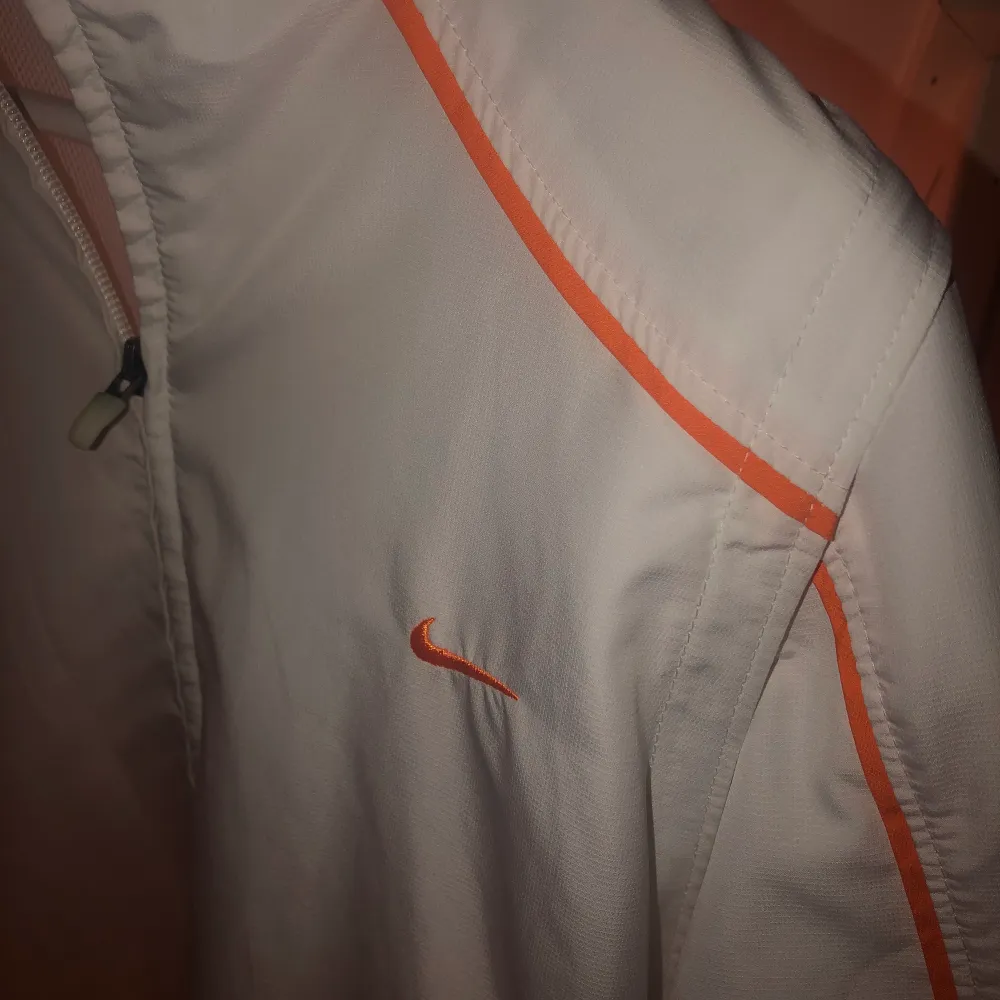 En vit sportjacka från Nike med orangea ränder. Jätte cool och väldigt bra skick. Frakt TILLKOMMER!. Jackor.