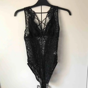  - Jätte fin svart spets body. Den är lite genomskinlig över bysten. Den har streck över bysten och även på ryggen. Den är låg i ryggen. Knäppning i grenen. Står storlek M men passar bättre på en S. I fint skick! 