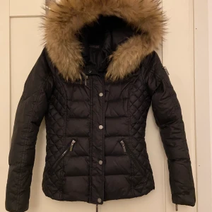 Rockandblue dunjacka,strl. 34 - Mycket fin dunjacka, Zora från ROCKANDBLUE som är en jacka av med en fyllning bestående av 80 % dun och 20 % fjäder, som dessutom är väldigt snygg! Den har en hood och en pälskrage, eller pälskant, och både hooden och kragen är avtagbara. Den avtagbara pälskragen är av äkta päls och mycket mjuk och skön. Quiltad på övre delarna av ärmarna, på axlarna och på sidorna.  Strl. 34. Bud från 2.000 kr.  Nypris ca 3.700 kr.  Finns på fler sidor.