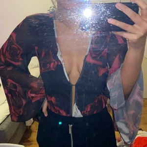 Snygg body med rosor - Säljer denna sjukt snygga body från Gina, den går att ha som andra bilden men de finns en knapp som gör de mindre urringat, den är sjukt snygg och ärmarna och ryggen är mesh så man ser lite igenom, de är fina rosor över hela och den ser jätte romantisk ut🥰 bodyn är string och den är i strl xs och använd 1 gång