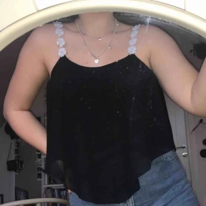  - Svart blus med blommiga axelremmar. Storlek och märke står ej men jag tror den är S. Knappt använd, kontakta om du är intresserad.