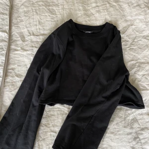Croppad svart tröja - Säljer denna jättefina och sköna croppade collegetröja från Monki. Den har också utsvängda armar. Säljs då den inte kommer till någon användning!