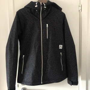 Skidjacka, svart med mönster  - Svart skidjacka med diskret leopardmönster, stl Small. Använd totalt två veckor, perfekt skick! Innerficka samt bröstficka att lägga mobil/skipass i. Förövrigt ytterligare två rymliga fickor. Köptes för 1500kr. Köpare står för eventuell frakt.