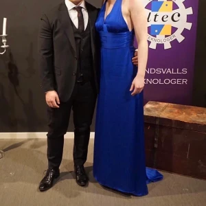 Aftonsklänning Storlek S - Blå, vacker aftonsklänning som passar lika bra på studentbal, som på bankettmiddagen eller som aftonsklänning vid annan sittning. V- ringad framtill, korsad i ryggen och ett litet släp på kjolen i bak. 