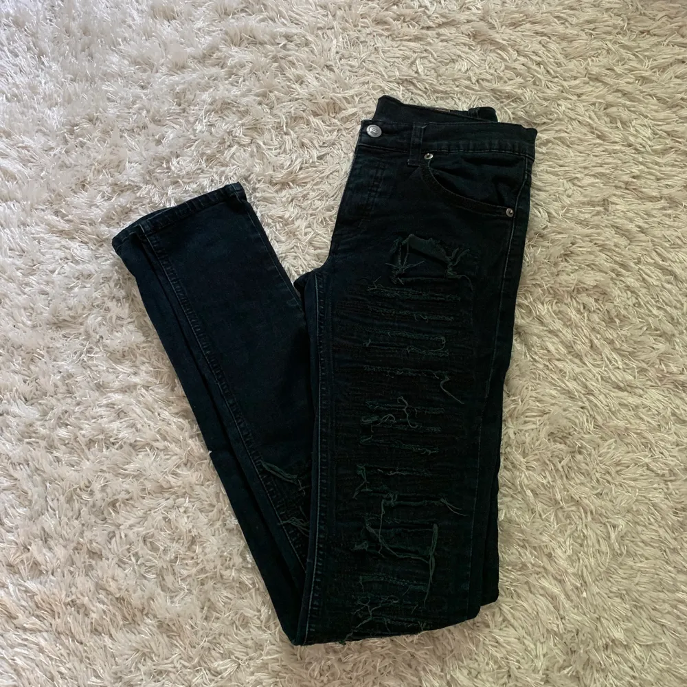 Snygga mörkblå tighta jeans med slitningar längs benen både bak och fram. Jeans & Byxor.