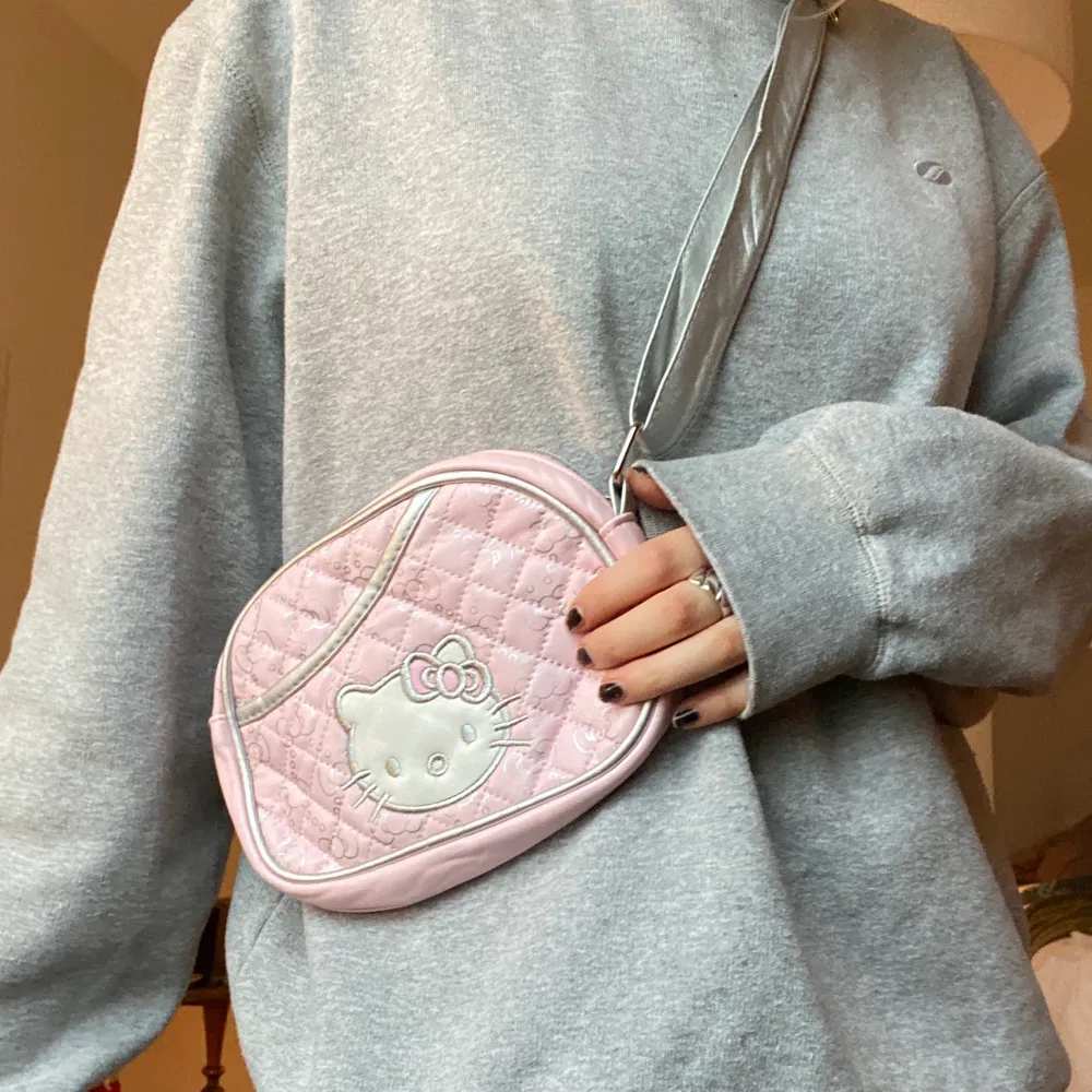 Justerbar Hello Kitty handväska! Ljusrosa med hello Kittys ansikte på ena sidan och ett justerbart silvrigt band! Köpt second hand, använt skick (små slitningar här och där på axelbandet). Frakt 22kr  . Väskor.