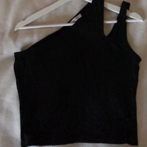 NAKD topp - Svart one shoulder topp från Nakd men snygg slits vid ena axeln, använd vid endast 1 tillfälle. Eventuell fraktkostnad tillkommer.