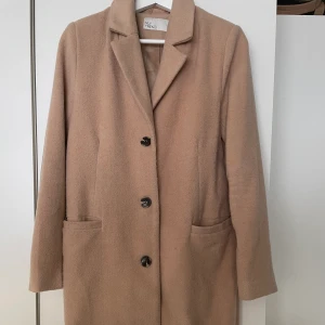 Beige Nelly Kappa - Jättetrendig beige kappa. Säljer pga bytt stil. Använd fåtal gånger. Nypris 700 kr. Högst budande!