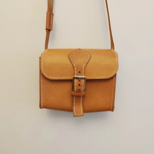 Handgjord väska i läder - Handgjord axelremsväska i läder från 90-talet. Helt oanvänd och i perfekt nyskick. Obehandlat naturläder i fin kvalité! Bredd 18cm Höjd 15cm