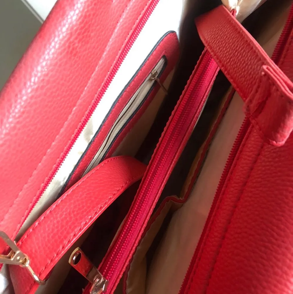 En röd handväska i (oäkta) läder med guldiga dragkedjor och smådetaljer. Axelrem medföljer. Aldrig använd. . Väskor.