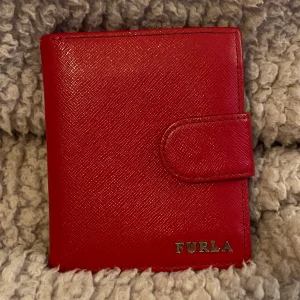 Furla Plånbok  - Fin röd plånbok med rött sidenmatt foder. Myntfack m blixtlås, många individuella fack för tex passerkort och kredit/betalkort. Slejf med tryckknapp. Bra använt skick och många år kvar att brukas. 