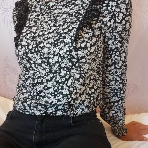 Blommig blus med volangaxlar - Supersöt med små rosaaktiga blommor 🌸 resår i slutet på ärmarna och knapp bak. Frakt ingår i priset!