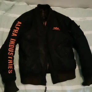 Alpha jacka  - Snygg alpha i väldigt bra skick. Avtagbar luva. Svart med orange text.  Kan mötas upp på bestämd plats i sthlm eller fraktas. 