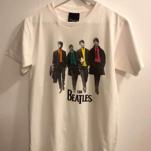 The Beatles T-shirt  - The Beatles Walking Down The Street t-shirt, stl Large. Från axel ner är den ca 69cm och på bredden från armhåla till armhåla är den ca 48cm. Den är ny och aldrig använd. Hämtas upp i Enskededalen. Har ca 5st kvar av denna. XL finns också några kvar av.