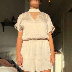  - Superfin playsuit från Ginatricot strl 36/S, aldrig använd. Färgen är champagne och materialet lite glansigt. Finns att mötas upp i centrala Stockholm. Kan även posta där köparen står för frakten.  