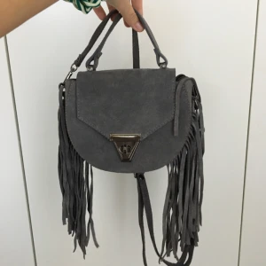  - Liten grå väska med fransar och dragkedja i mycket bra skick. Använd fåtal gånger. Du betalar frakten :)